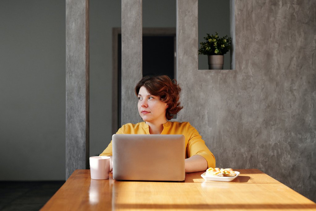 Dame zittend aan tafel met haar laptop, koffiemok en ontbijt