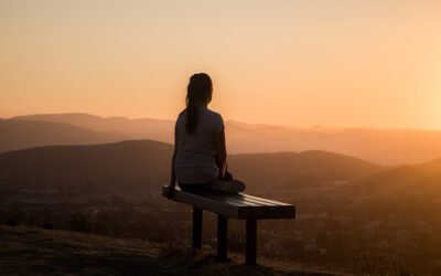A women sat on a bench looking out at the view of hills during a sunrise