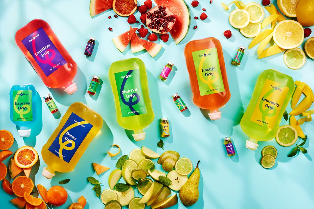 meerdere IV Drip flessen en Booster shots op een blauwe achtergrond omringd door fruit