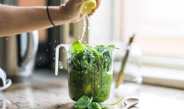 A jug of spinach and someone is squeezing lemon on top.