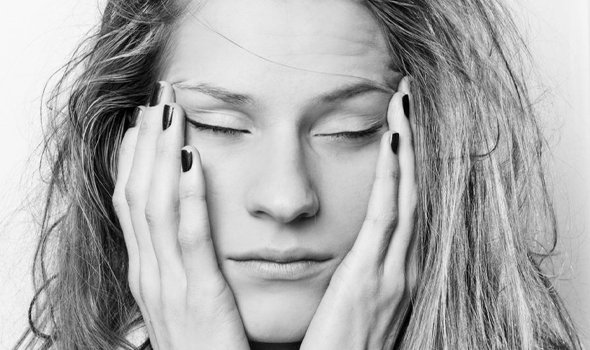 A woman who looks tired and stressed with he hands on her face