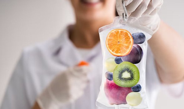A woman holding an IV Drips bag containing a slice of orange, kiwi, apple, plum and blueberry's